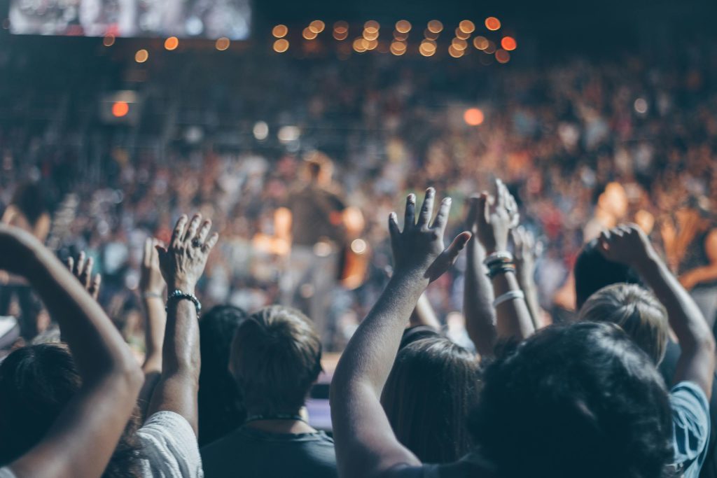 Energetic crowd at a live concert with hands raised and bright lights.